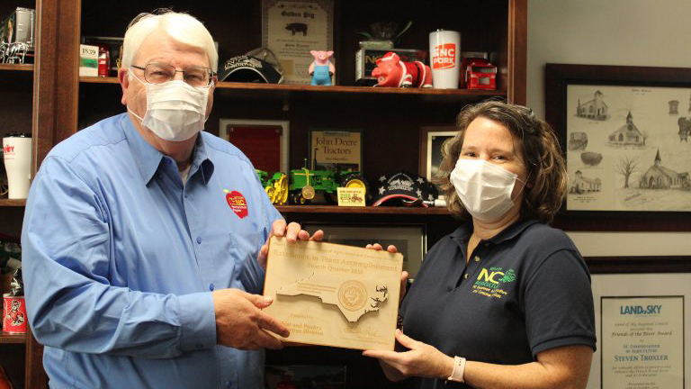 Karen Beck and Steve Troxler in masks holding a plaque